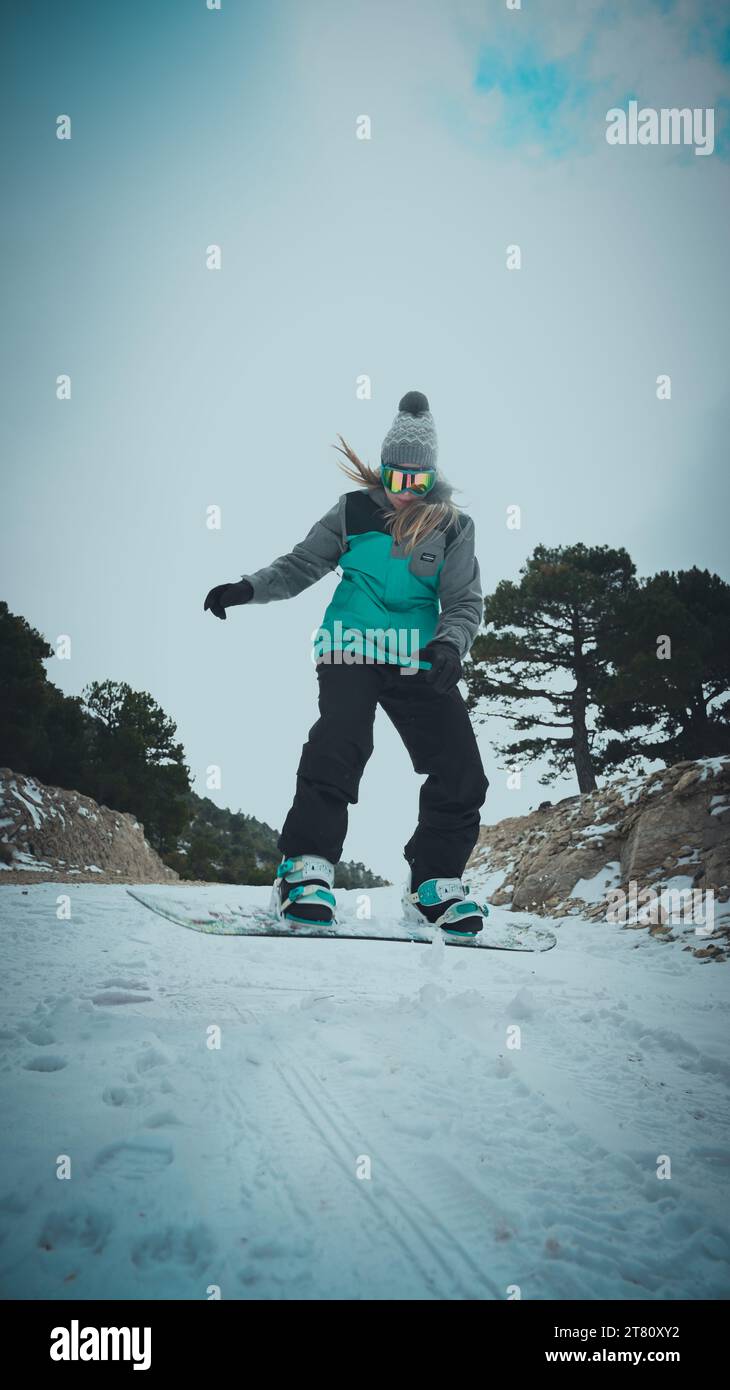 Eine Snowboarderin gleitet einen unberührten weißen Hügel hinunter und blickt mit einem entschlossenen Ausdruck in den Himmel Stockfoto