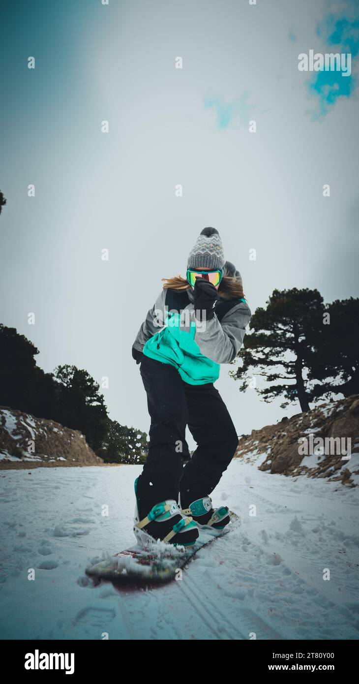 Eine Sportlerin mit Schutzbrille und Wintermantel, während sie im Winter einen Berghang hinunterboardet Stockfoto