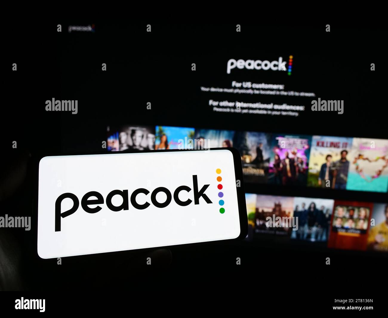 Person, die ein Smartphone mit dem Logo des US-amerikanischen Videostreaming-Unternehmens Peacock TV LLC vor der Website hält. Schwerpunkt auf dem Display des Telefons. Stockfoto