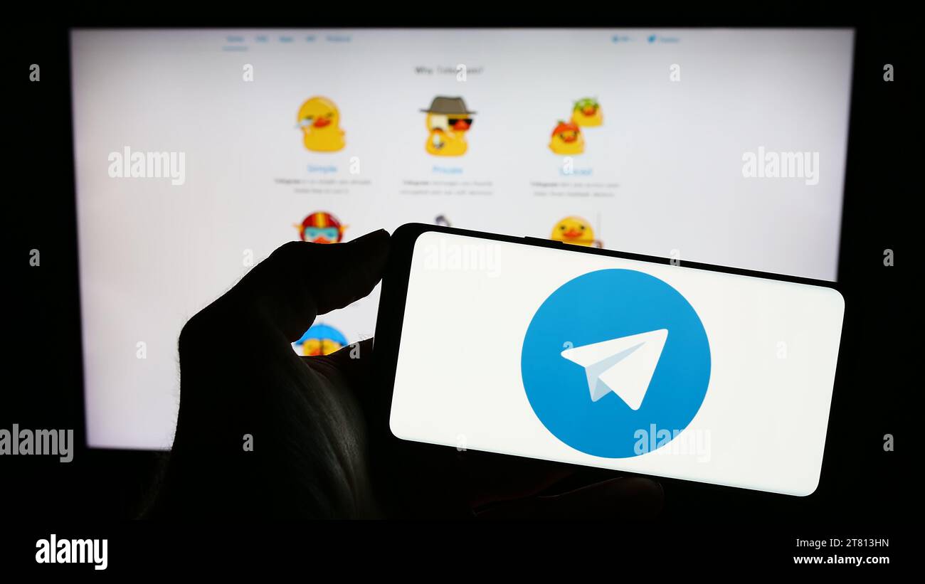 Person, die ein Mobiltelefon mit dem Logo des Instant Messaging-Dienstes Telegram Messenger vor der Webseite hält. Schwerpunkt auf dem Display des Telefons. Stockfoto