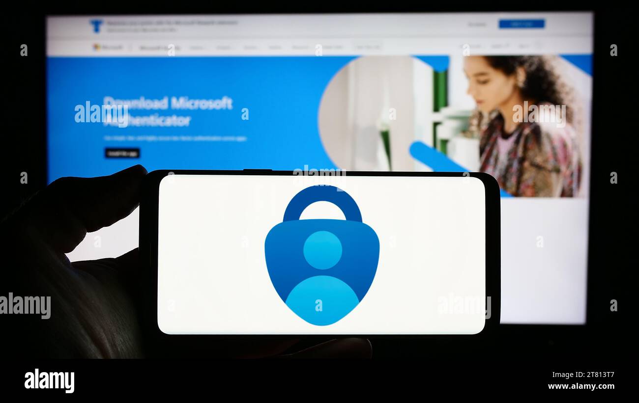 Person, die ein Mobiltelefon mit dem Logo der Authentifizierungs-App Microsoft Authenticator vor der Unternehmenswebsite hält. Schwerpunkt auf dem Display des Telefons. Stockfoto