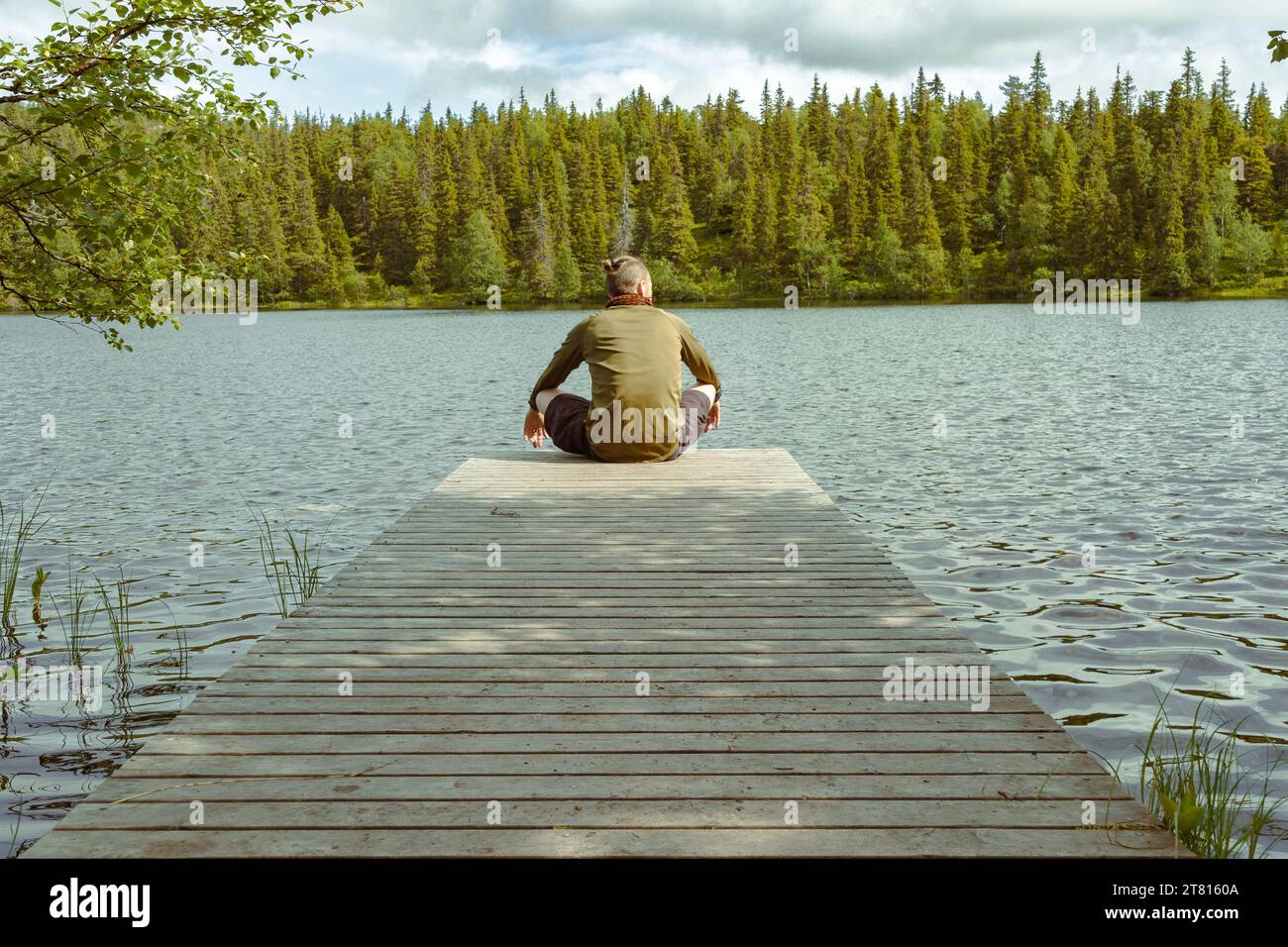Ein Mann ruht sich am Ende eines privaten Stegs während einer langen Wanderung im Wald in Finnland aus Stockfoto
