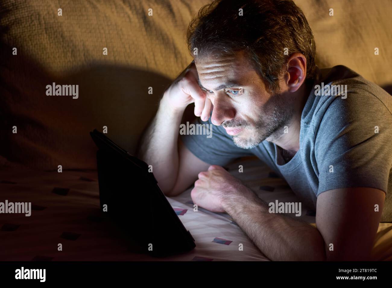Junger gutaussehender Mann, der nachts im Bett liegt und etwas auf einem Tablet sieht. Kopierbereich für Text. Stockfoto