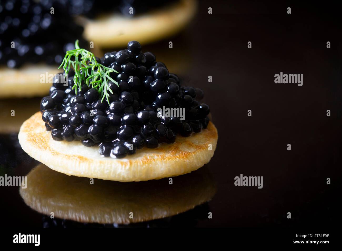 Nahaufnahme von schwarzen Kaviar-Blinis mit frischem Dill auf schwarzem Hintergrund mit Kopierraum. Stockfoto