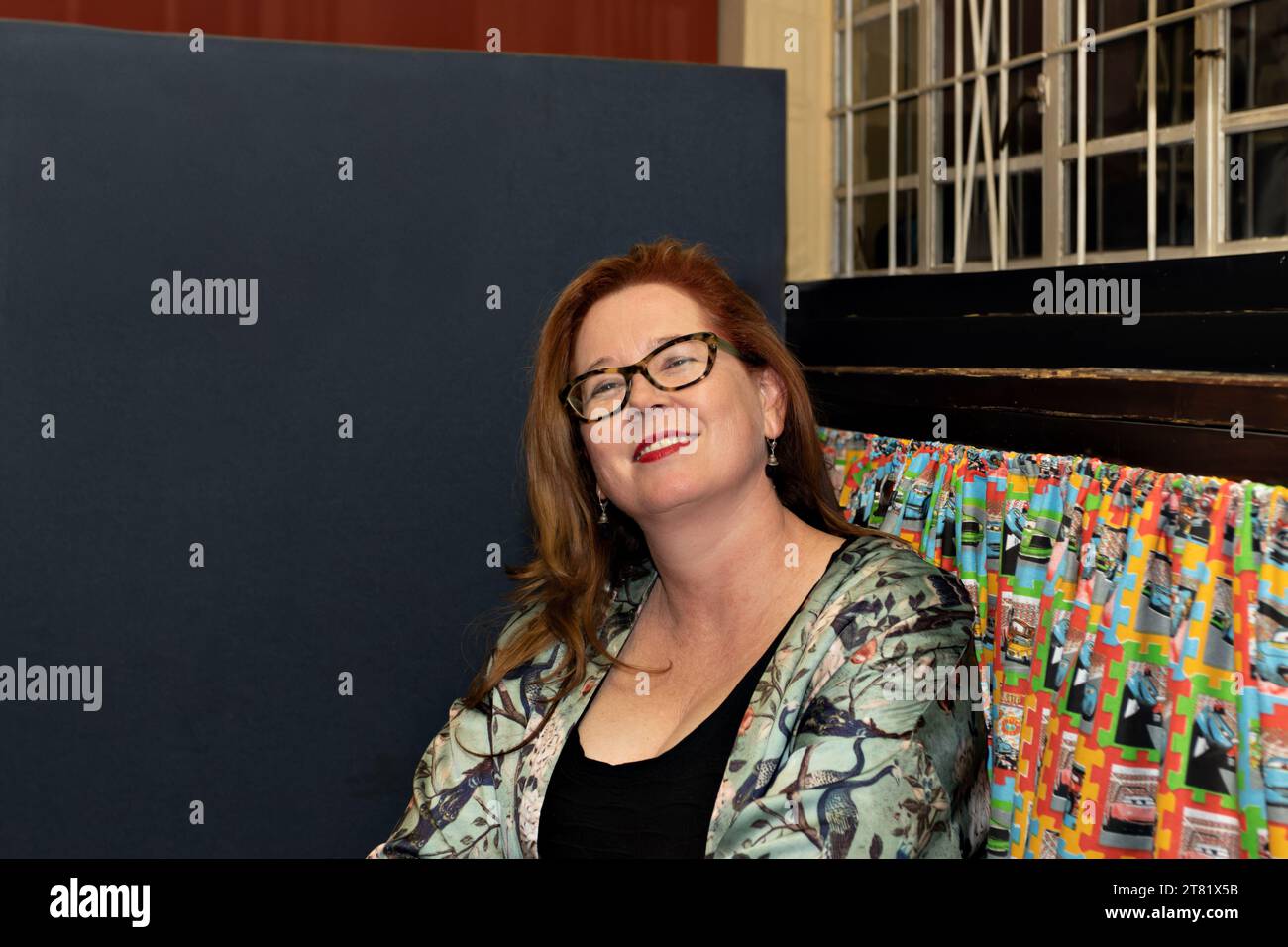 südafrikanische Rothaarige Frau mit lächelnder Brille, drinnen im Fenster mit Einbrecherriegeln Stockfoto
