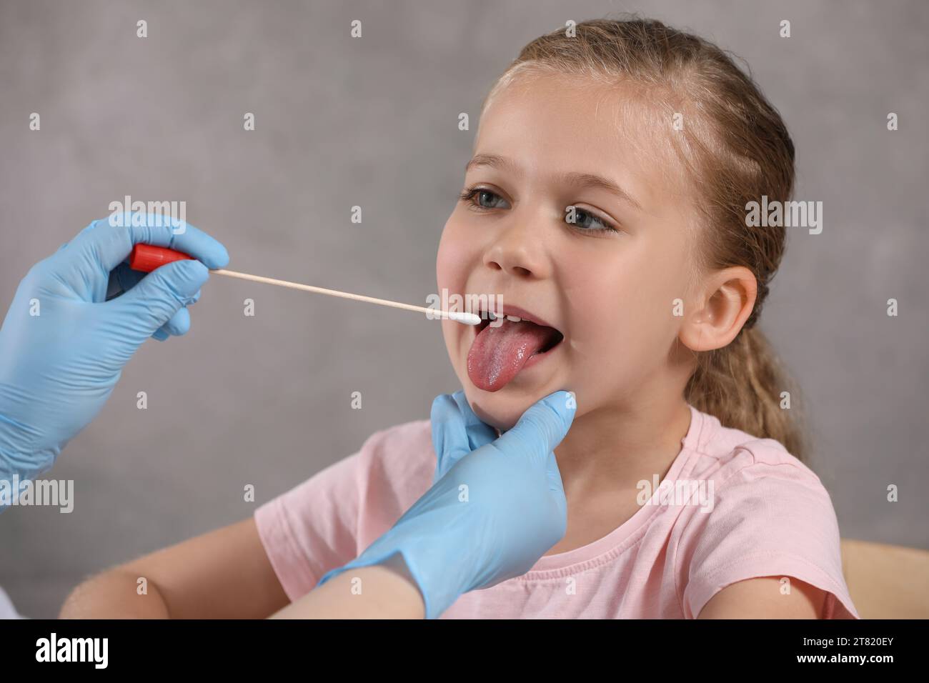 Doktor nimmt eine Rachenabstrichprobe aus der Mundhöhle des Mädchens auf grauem Hintergrund, Nahaufnahme Stockfoto