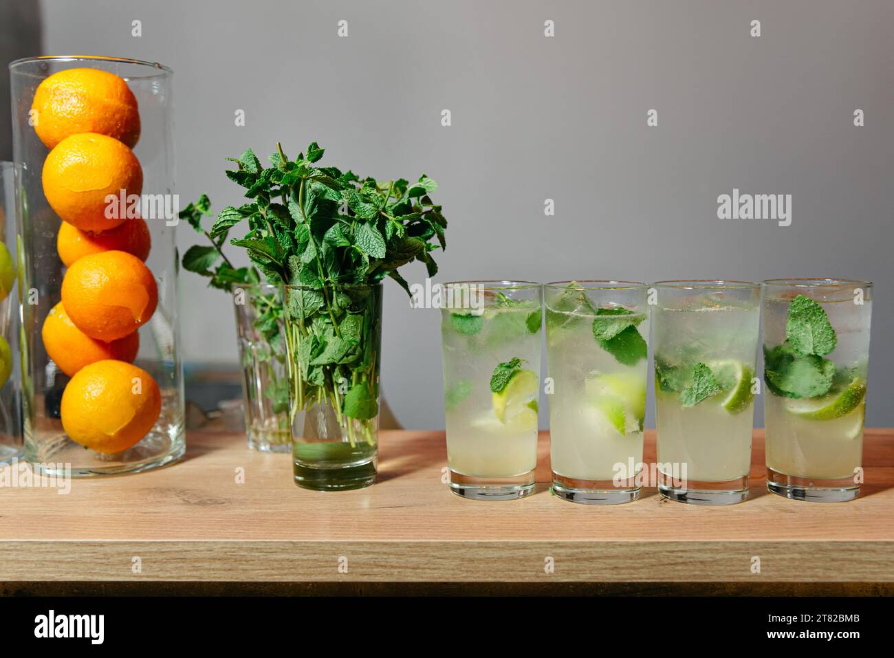 Gläser mit köstlichen Mojito-Getränken, geschmückt mit Limettenkeilen, Eiswürfeln und Minzblättern. Die lebhafte Bar-Szene umfasst eine Vase mit Orangen und ein Glas Stockfoto