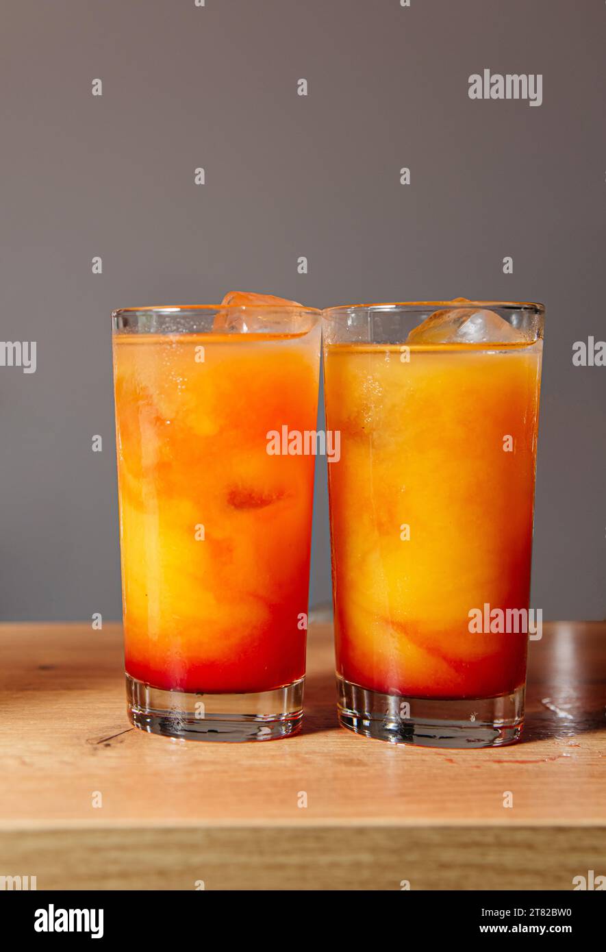 In Highball-Gläsern werden lebhafte Tequila Sunrise-Cocktails an einer Bar präsentiert. Erfrischende Orangentöne mit Eiswürfeln. Stockfoto