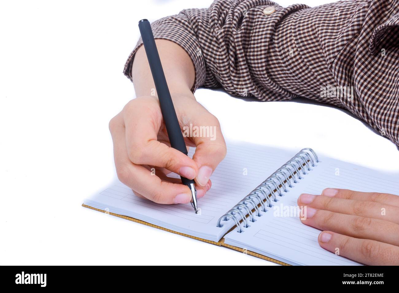 Eine Kinderhand ist auf eine Spiral-Notizbuch auf weißem Hintergrund mit Stift schreiben. Stockfoto