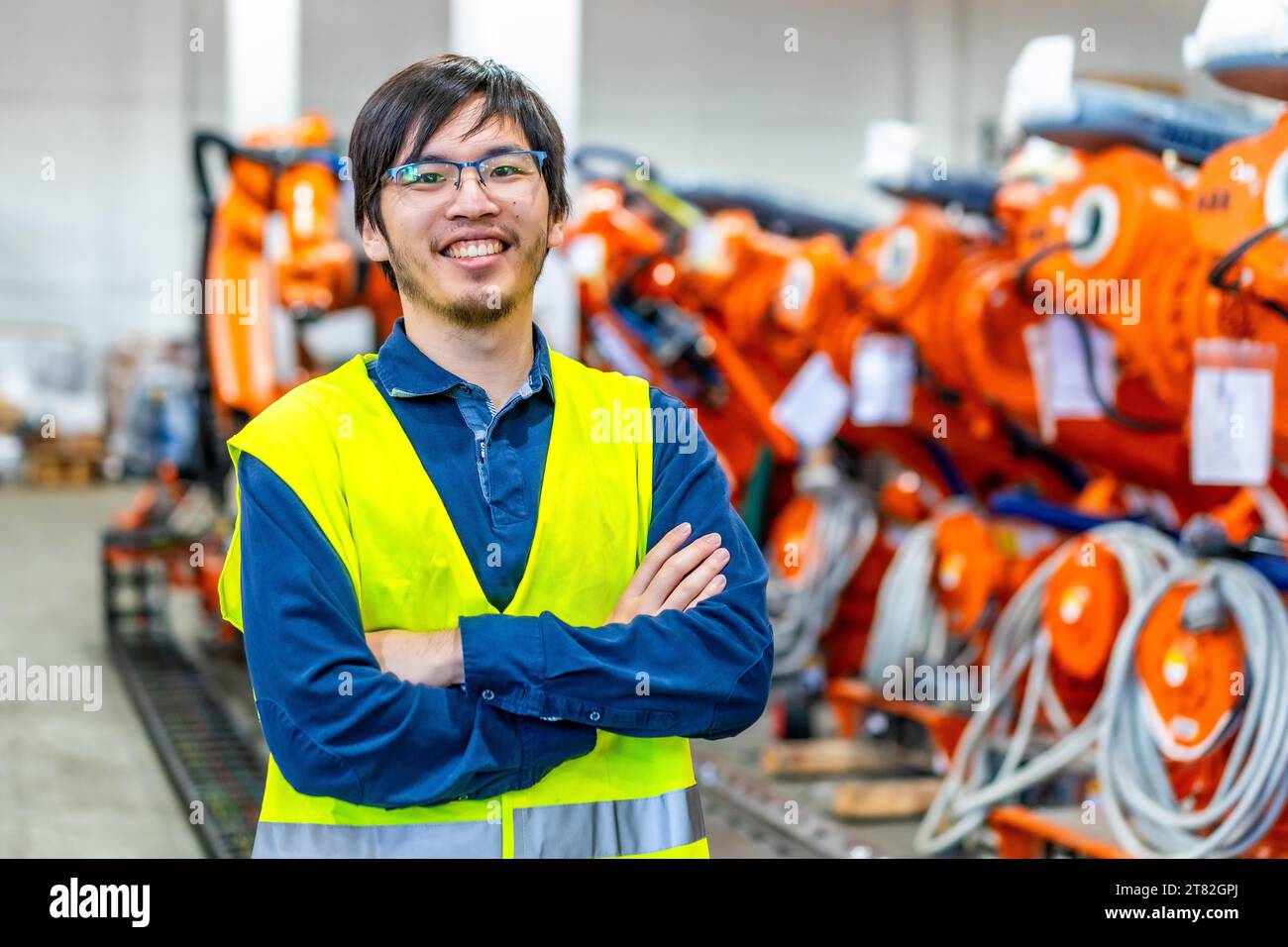 Stolzer japanischer Chefingenieur einer Roboterindustrie, der mit gekreuzten Armen neben der Montagelinie steht Stockfoto