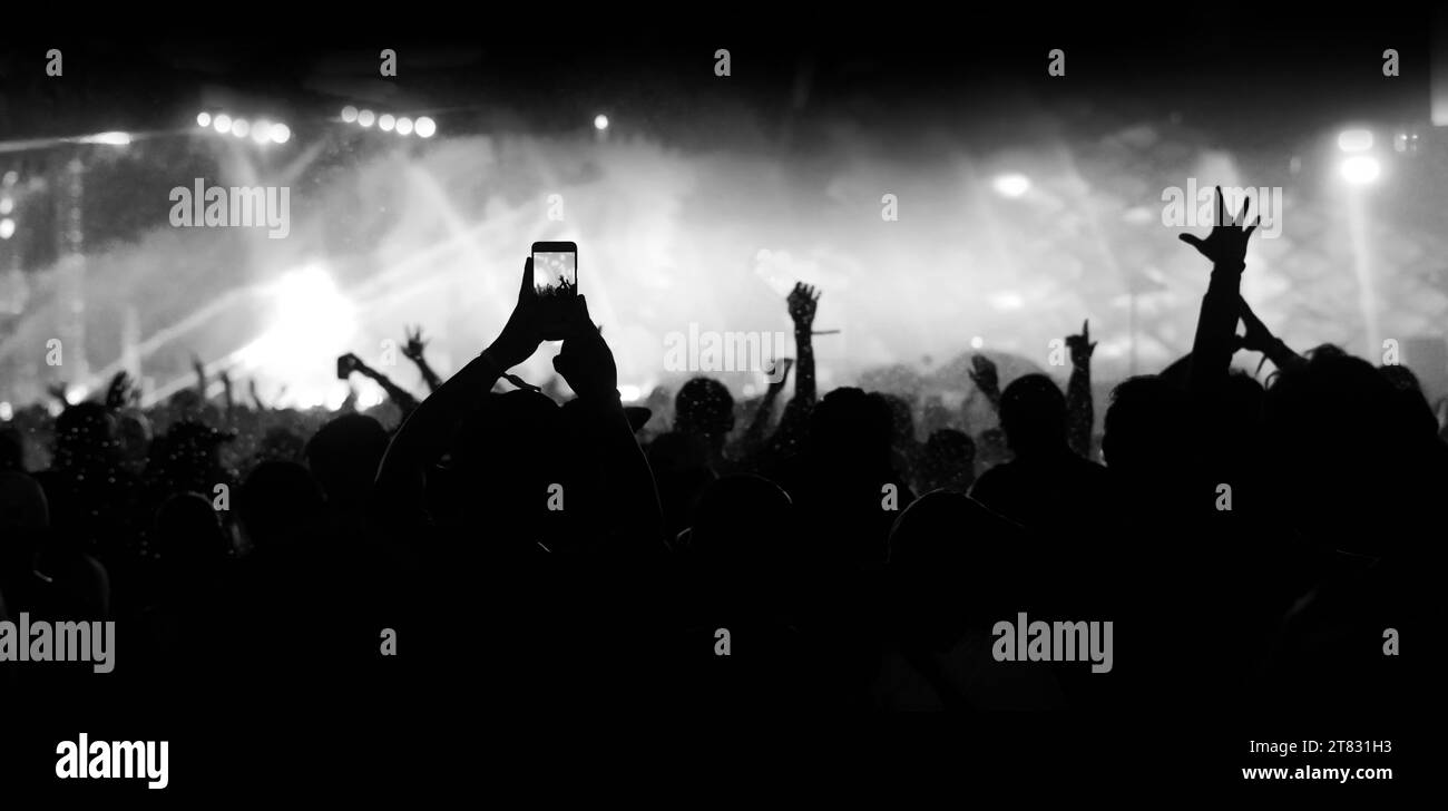 Die Menge auf einem Konzert. Spaß, Hände hoch und halten Sie einen Moment mit dem Smartphone fest. Schwarz-weiß-Technik. Stockfoto