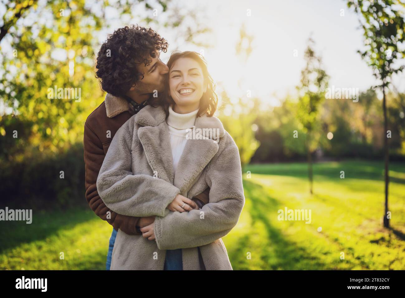 Glückliches, liebevolles Paar, das sich bei Sonnenuntergang im Park umschließt und küsst. Stockfoto