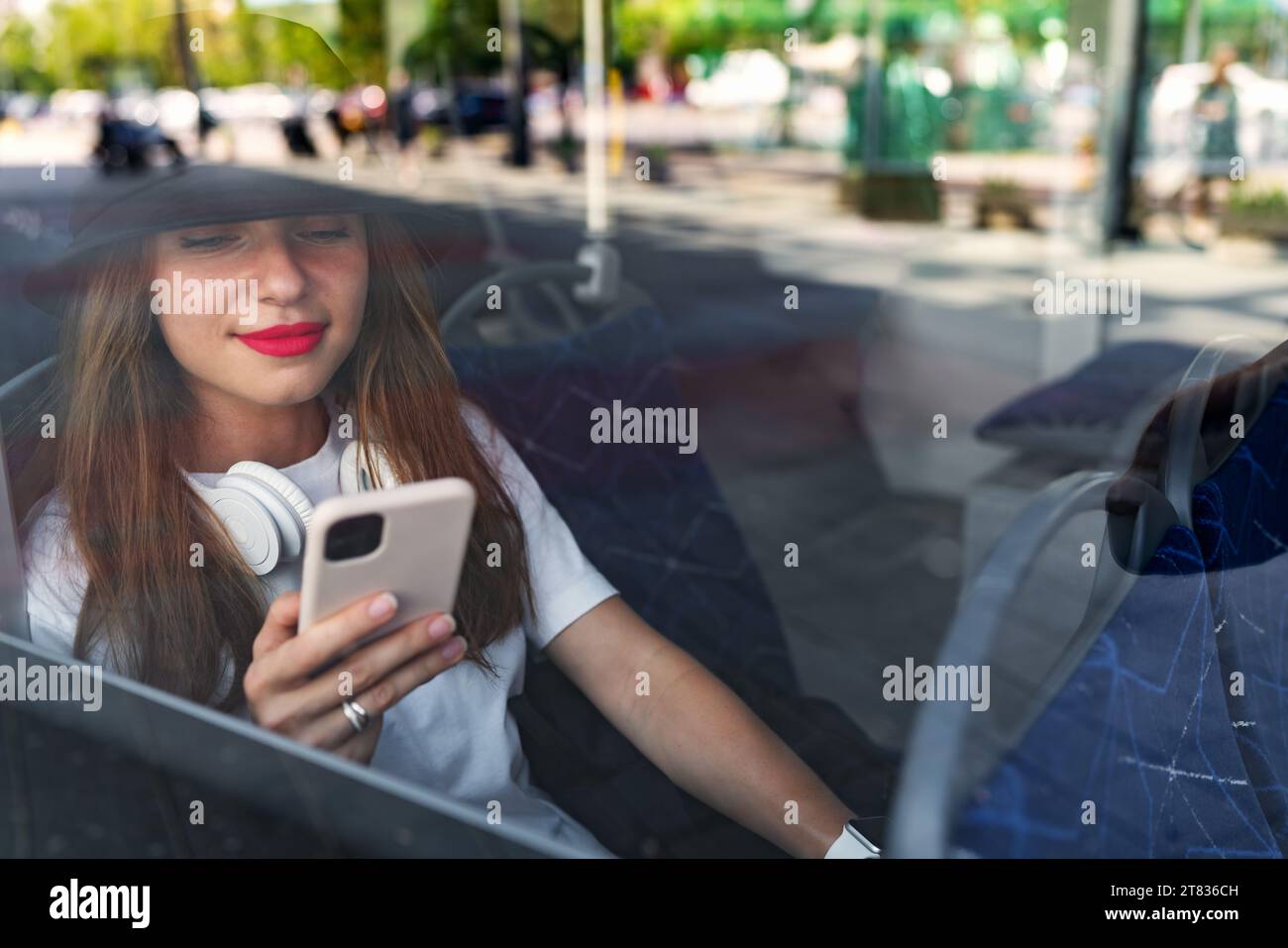 Foto durch das Glas des Busfensters, Passagierin, die ihr Smartphone benutzt, während sie im Shuttlebus sitzt. Stockfoto