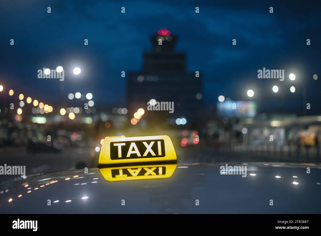 Selektiver Fokus auf gelbes Taxischild. Reflexion im Autodach gegen Flughafenterminalgebäude bei Nacht. Stockfoto