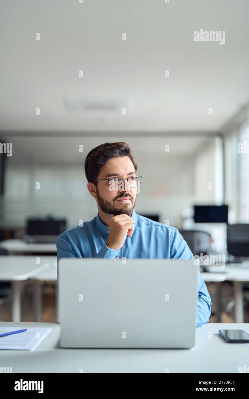 Durchdachter Geschäftsmann, der im Büro an einem Notebook arbeitet. Vertikale Aufnahme. Stockfoto