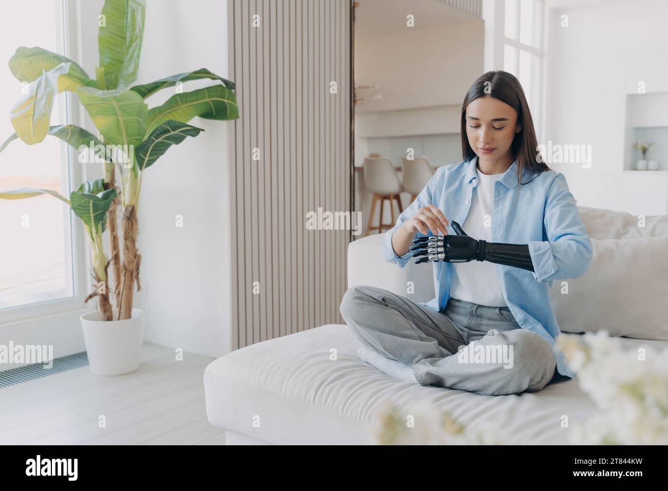 Eine ruhige Frau mit bionischem Arm sitzt bequem zu Hause und zeigt die Harmonie zwischen Technologie und Alltag Stockfoto