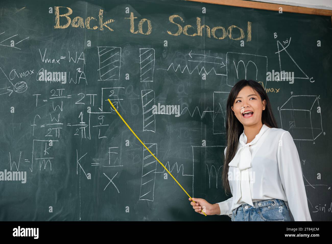 Asiatische Lehrerin lächelt mit Holzstab, der auf die Tafel zeigt Stockfoto
