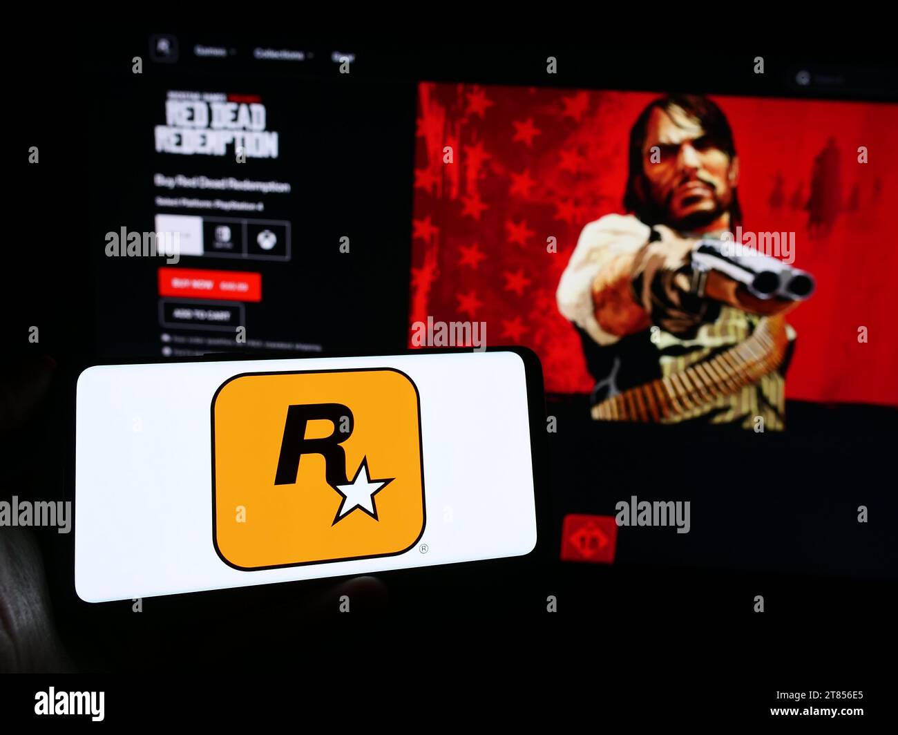 Person, die ein Mobiltelefon mit dem Logo des US-amerikanischen Videospielverlags Rockstar Games Inc. Vor der Unternehmenswebseite hält. Schwerpunkt auf dem Display des Telefons. Stockfoto