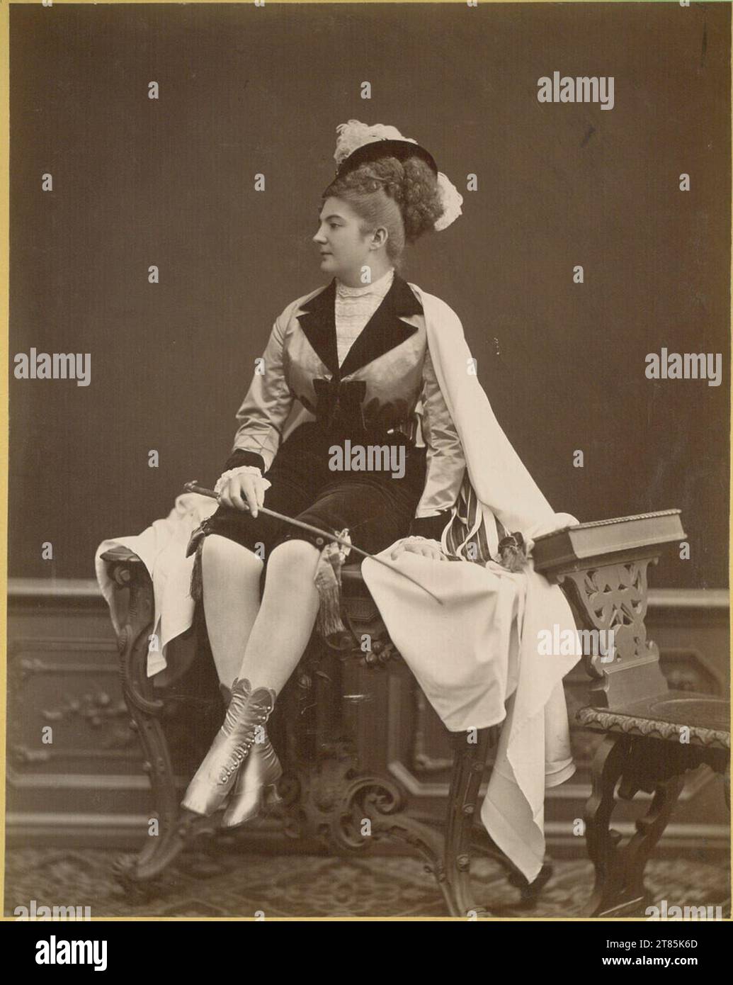 Julius Gertinger Porträt einer Schauspielerin in Hosenrolle mit Federhut, ganze Figur, sitzt auf einem geschnitzten Tisch. Albuminpapier, auf der Schachtel nach 1872 Stockfoto