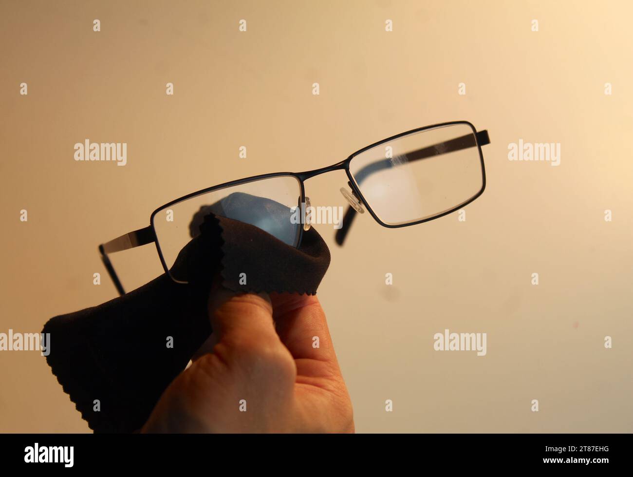 Ein Nahfoto von jemandem, der seine Brille mit einem schwarzen Mikrofasertuch abwischt. Stockfoto