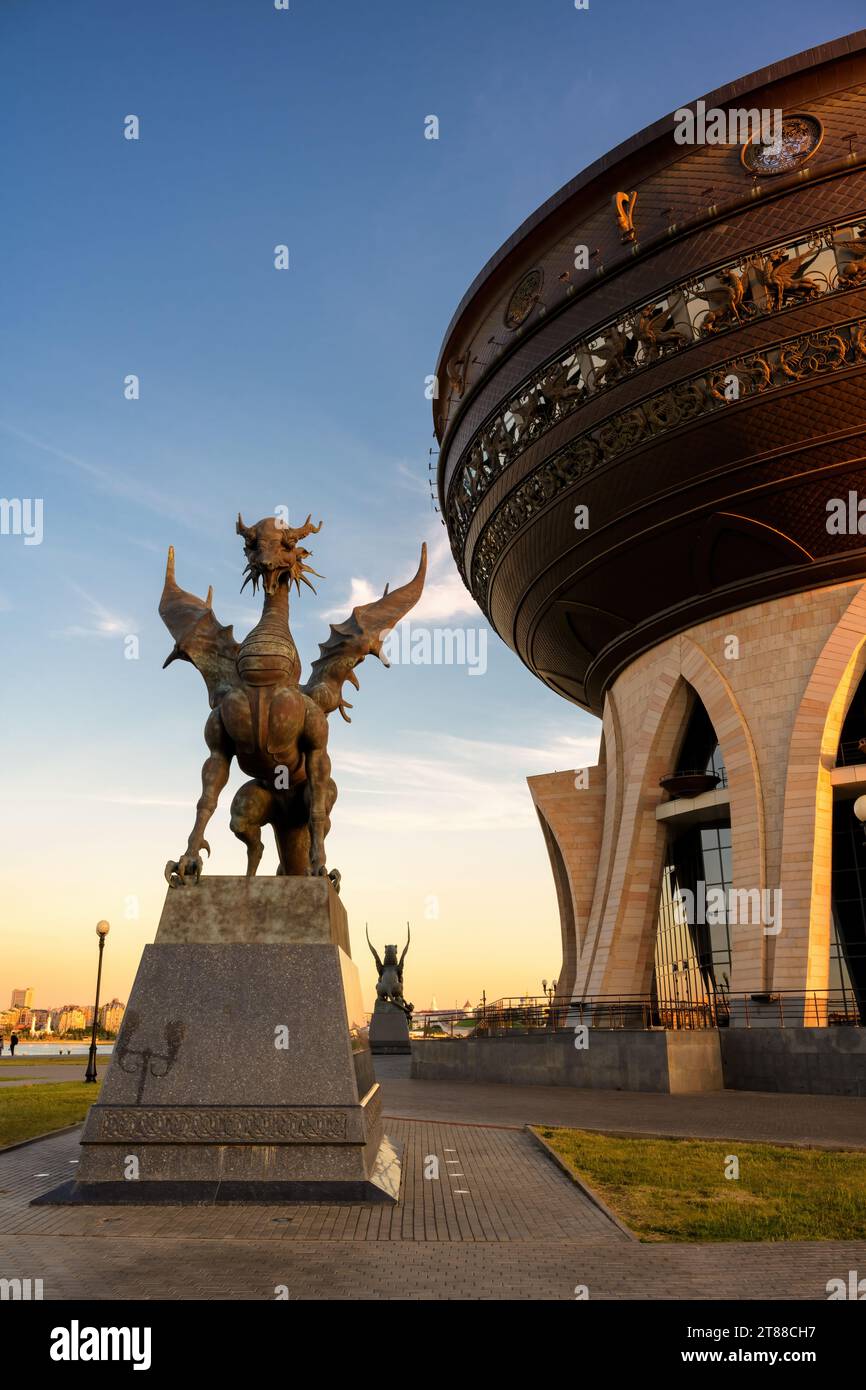 Hochzeitspalast und Drachenstatue bei Sonnenuntergang in Kasan, Tatarstan, Russland. Vertikaler Blick auf riesige Schüssel, Himmel und moderne Skulpturen, Wahrzeichen der Stadt. Design Stockfoto