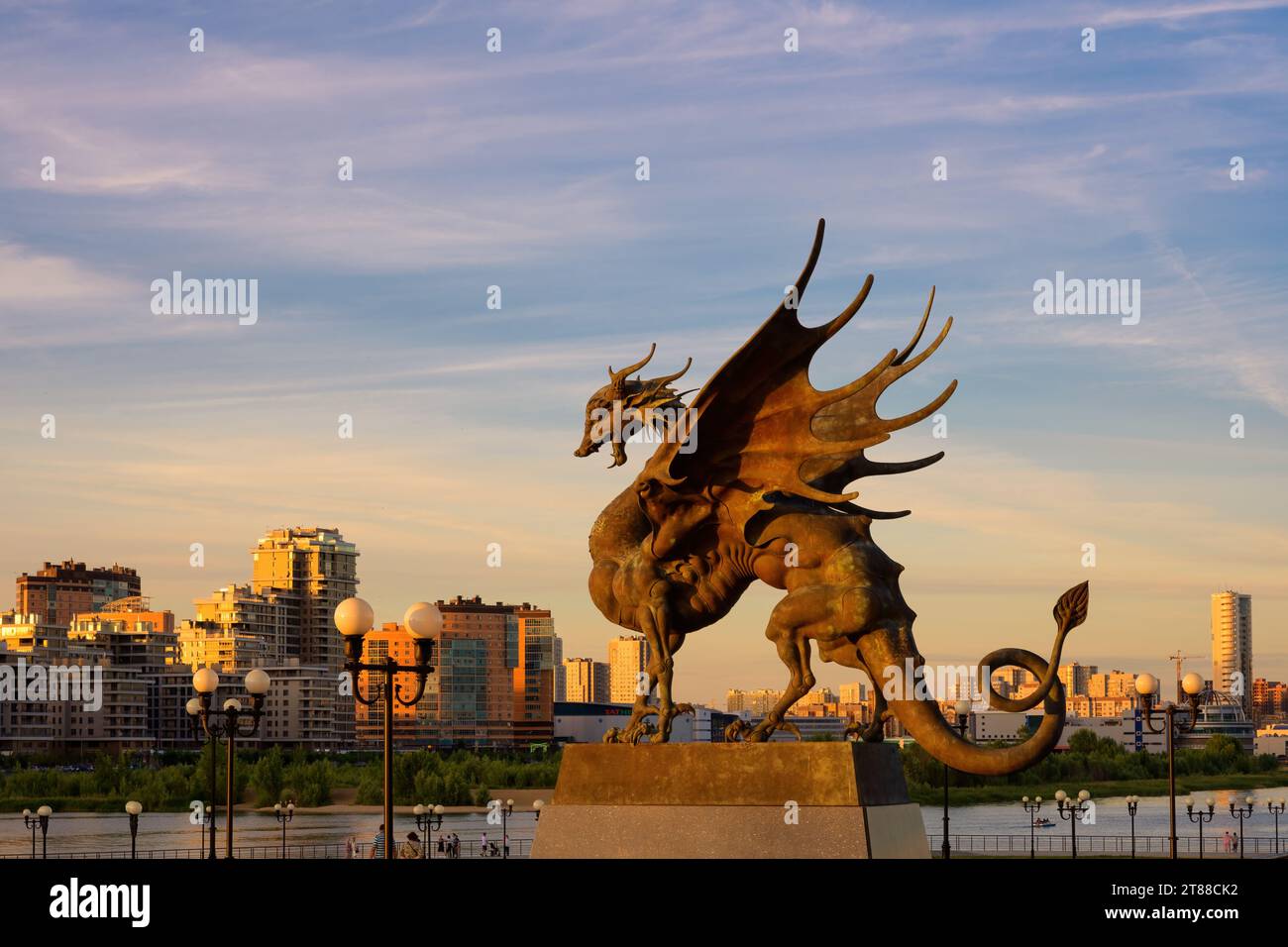 Drachenstatue auf dem Hintergrund des Himmels und der Gebäude bei Sonnenuntergang in Kasan, Tatarstan, Russland. Urbane Landschaft mit Skulpturen, Wahrzeichen der Stadt. Thema von Rus Stockfoto