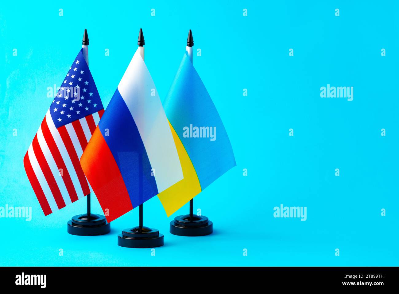 Kleine Fahnen von Russland, der Ukraine und den USA auf blauem Hintergrund Stockfoto