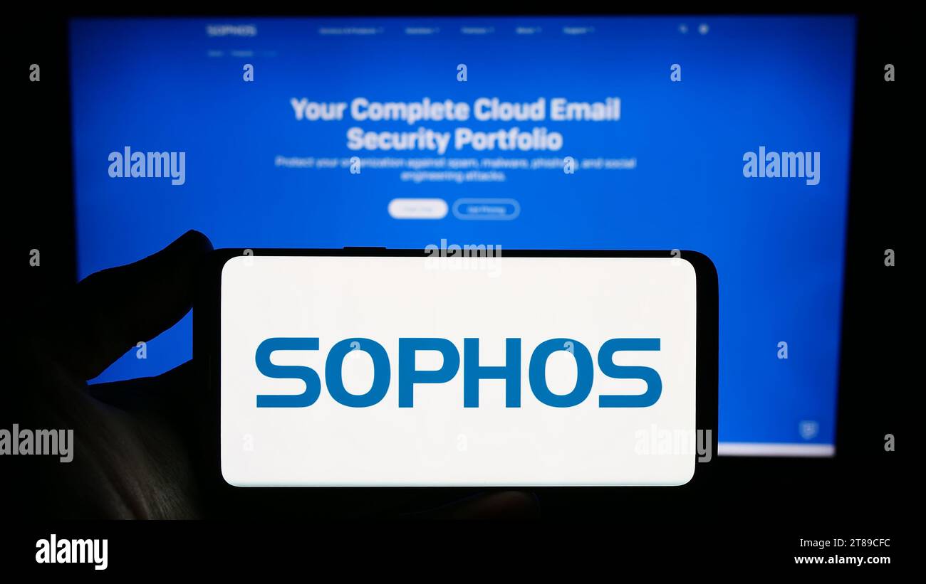 Person mit Smartphone und Logo des britischen Sicherheitssoftware-Unternehmens Sophos Group plc vor der Website. Schwerpunkt auf dem Display des Telefons. Stockfoto
