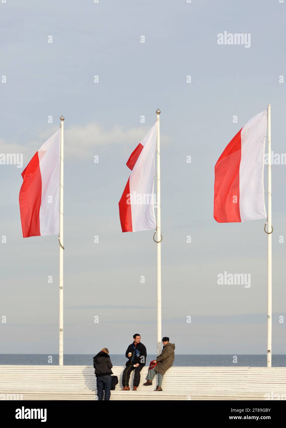 Polnische Nationalflaggen und asiatische Touristen am Sopot Pier außerhalb der Saison an einem kalten, sonnigen Wintertag in Sopot, Pommern, Polen, Europa, EU Stockfoto