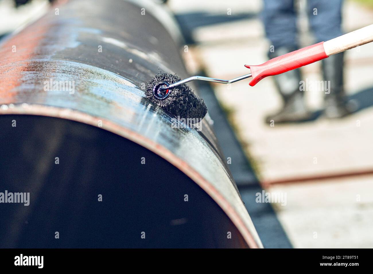 Metallrohr wird mit Lackierwalze mit schwarzer Farbe oder Bitumen lackiert. Schutz von Metallrohren vor Korrosion. Herstellung von Vergasungsrohren. Stockfoto