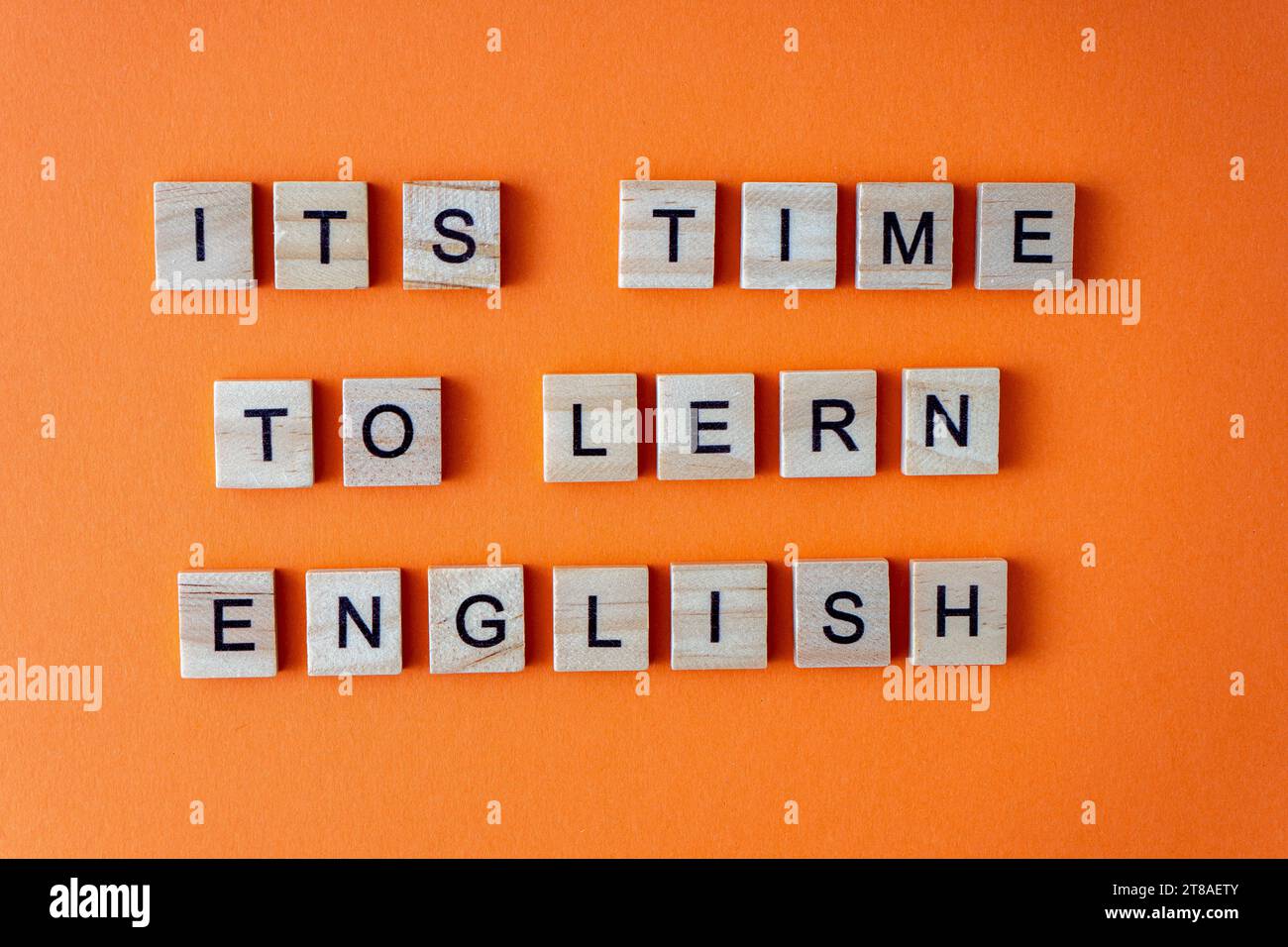 Es ist Zeit, Englisch zu lernen. Motivation. Der Satz ist in Holzbuchstaben von oben angeordnet. Motivation. Orangefarbener flacher Lay-Hintergrund Stockfoto