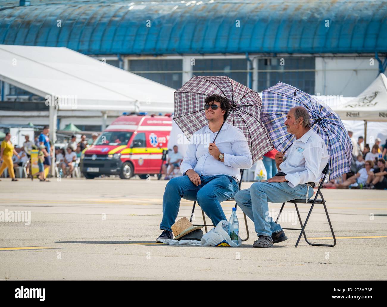 Bukarest, Rumänien, 25. August 2023: Zwei Männer mit Sonnenschirmen sitzen auf Stühlen in der Sonne. Sommer-Wärmekonzept. Stockfoto