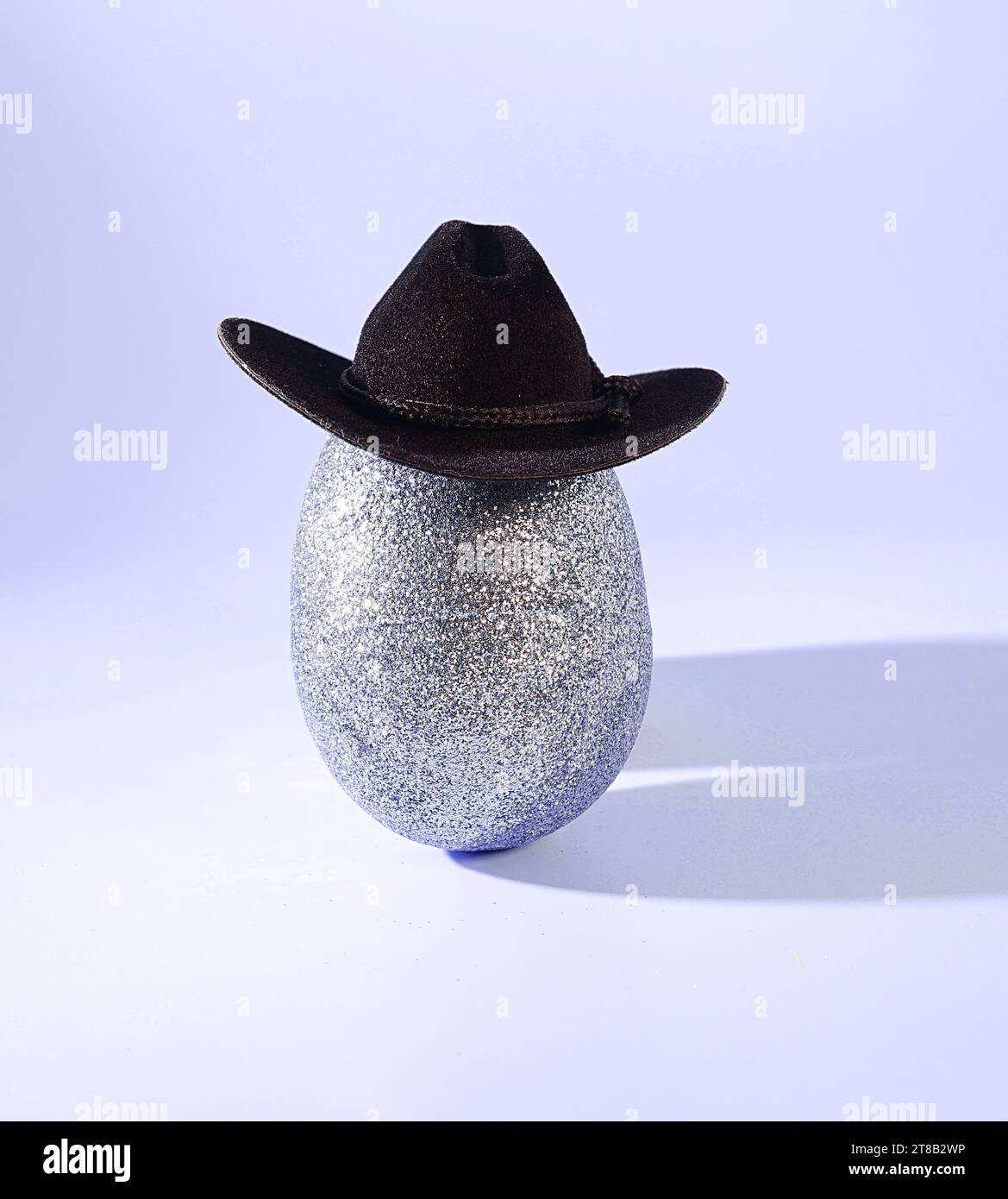 Easter Goes West: Ein glamouröses silbernes Osterei mit Glitzereffekt, das einen Cowboy Hut auf einem pastellfarbenen Hintergrund trägt Stockfoto