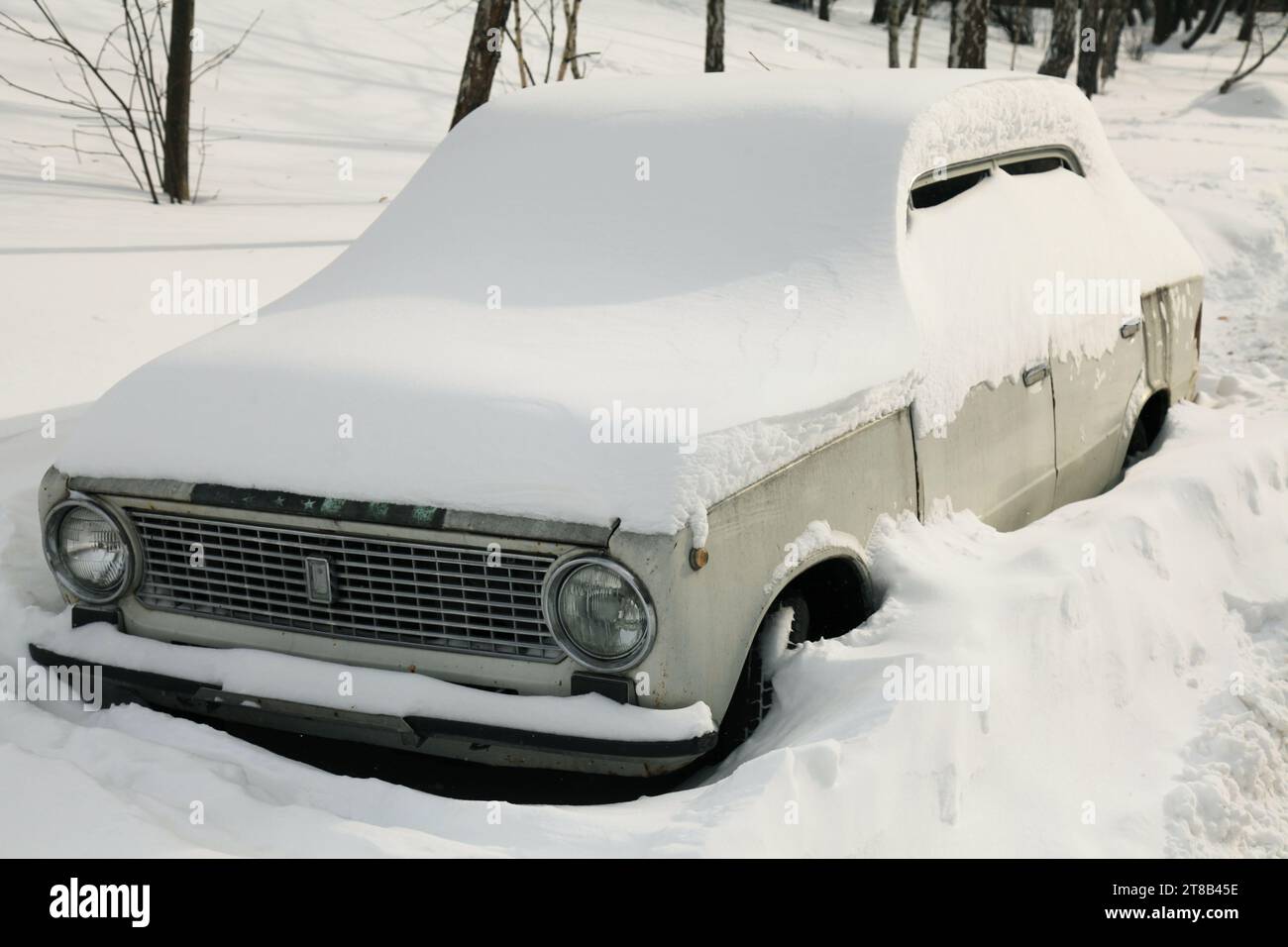 Schneebedeckter Winter in einer Großstadt. Ein altes Auto, das von einer riesigen Schneelage bedeckt war. Ungewöhnliches Wetter im Winter. Schneefall und Neujahr. Gelähmter Verkehr. Eiszeit Stockfoto