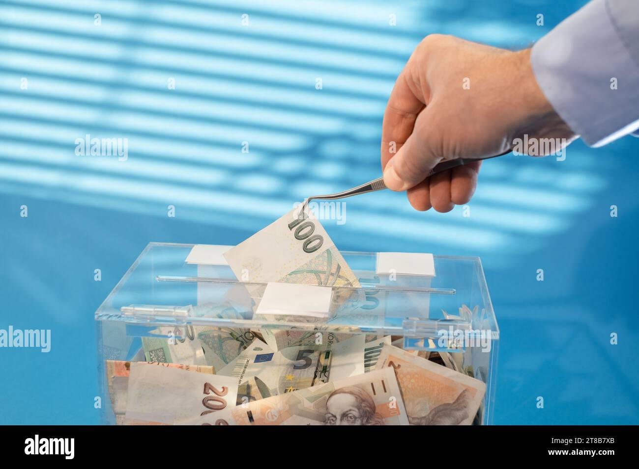 Der Akt des Diebstahls von Spenden. Eine Hand holt die tschechische Kronen-Banknote aus einer Spendenbox mit einer Pinzette. Stockfoto