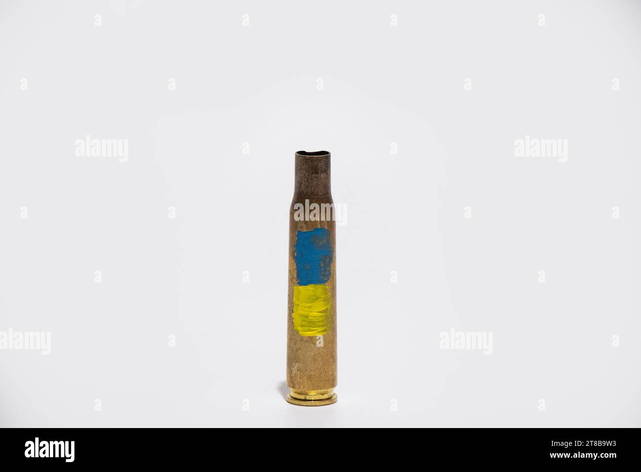 Gebrauchte Maschinengewehrgehäuse und die Flagge der Ukraine auf dem Gehäuse auf weißem Hintergrund gemalt, Waffen und Munition in der Ukraine Stockfoto