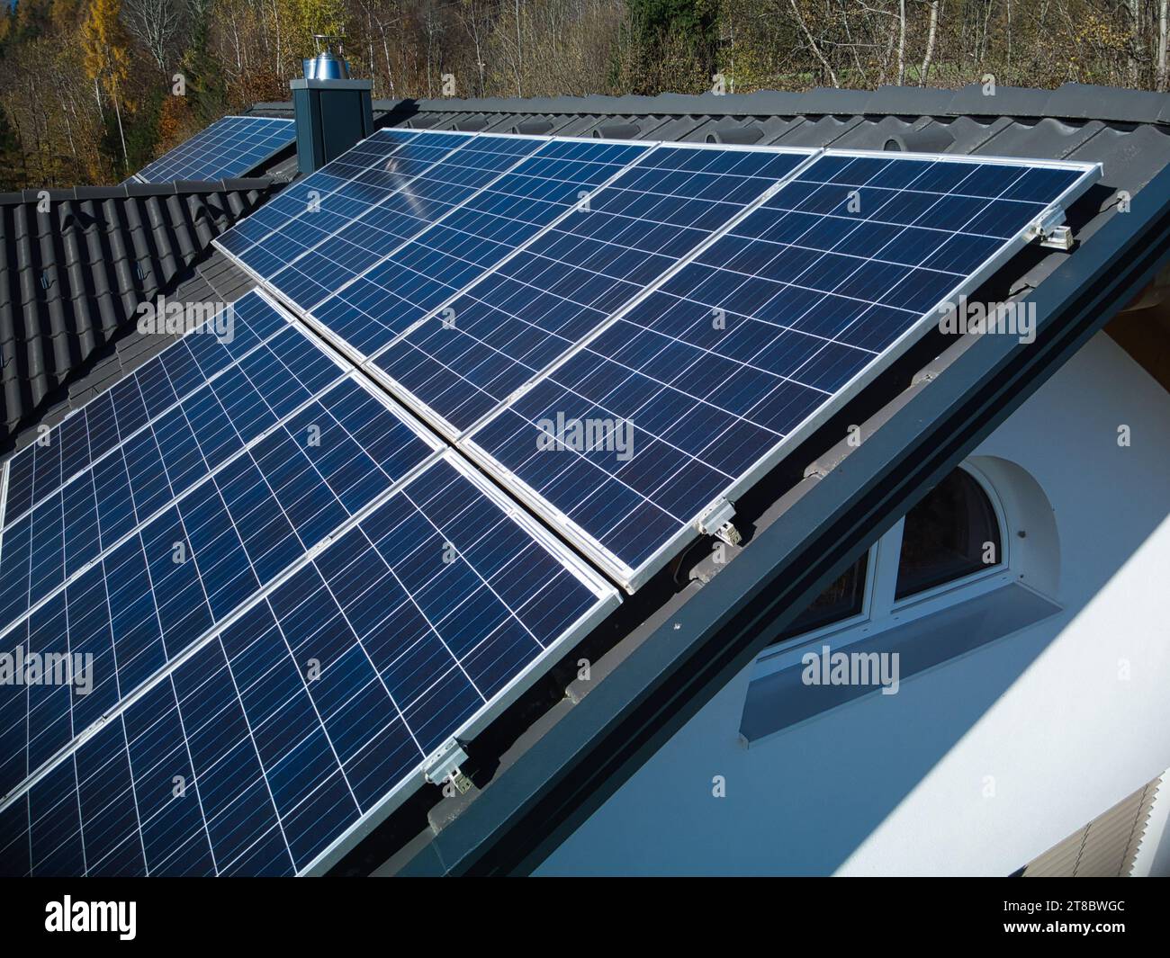 Erkunden Sie die komplexen Details erneuerbarer Energien mit dieser Nahaufnahme der Drohne, die PV-Panels auf einem dunklen Dach vor dem Hintergrund des lebendigen Au erfasst Stockfoto