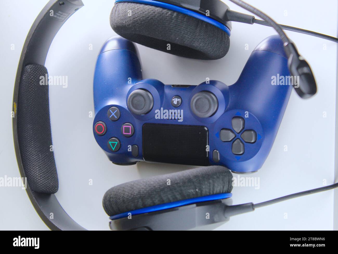 Ein Foto von einem dunkelblauen PlayStation-Spielekonsolen-Controller und zwei Kopfhörern auf einem weißen Tisch. Gamer. Stockfoto