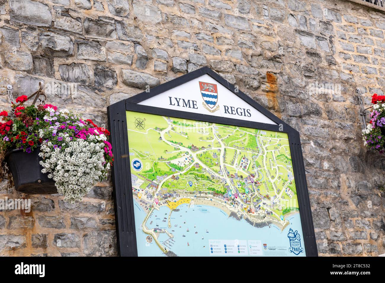 Lyme Regis Dorset Küste, Stadtplan und Informationstafel an einer Wand zwischen hängenden Körben befestigt, England, Großbritannien, 2023 Stockfoto