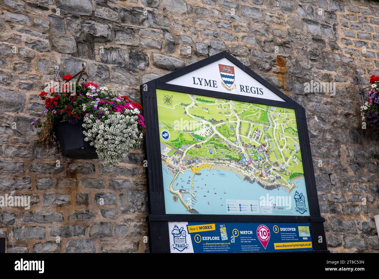 Lyme Regis Dorset Küste, Stadtplan und Informationstafel an einer Wand zwischen hängenden Körben befestigt, England, Großbritannien, 2023 Stockfoto