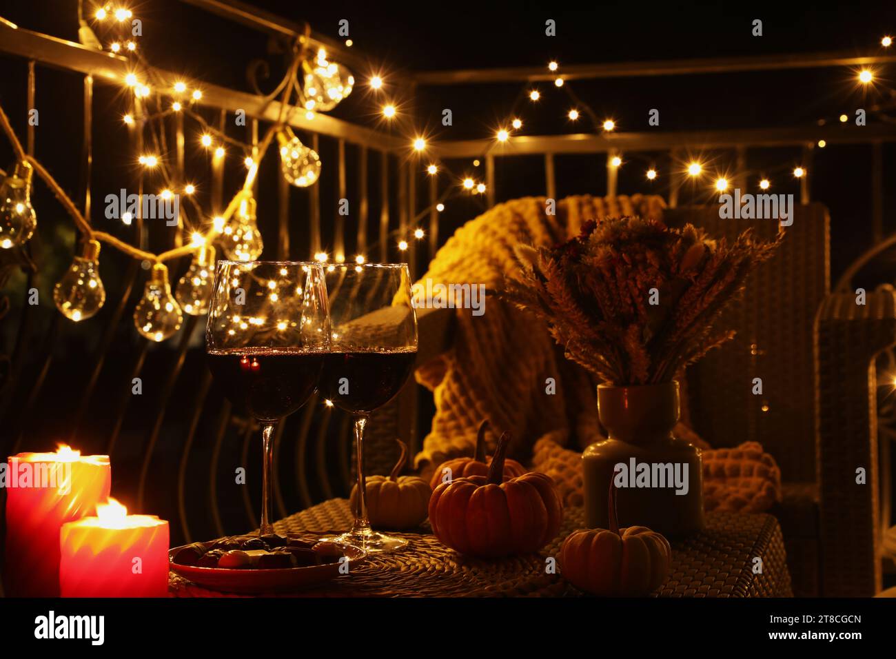 Weingläser, brennende Kerzen und Dekor auf Rattantisch. Herbstabend auf der Terrasse Stockfoto