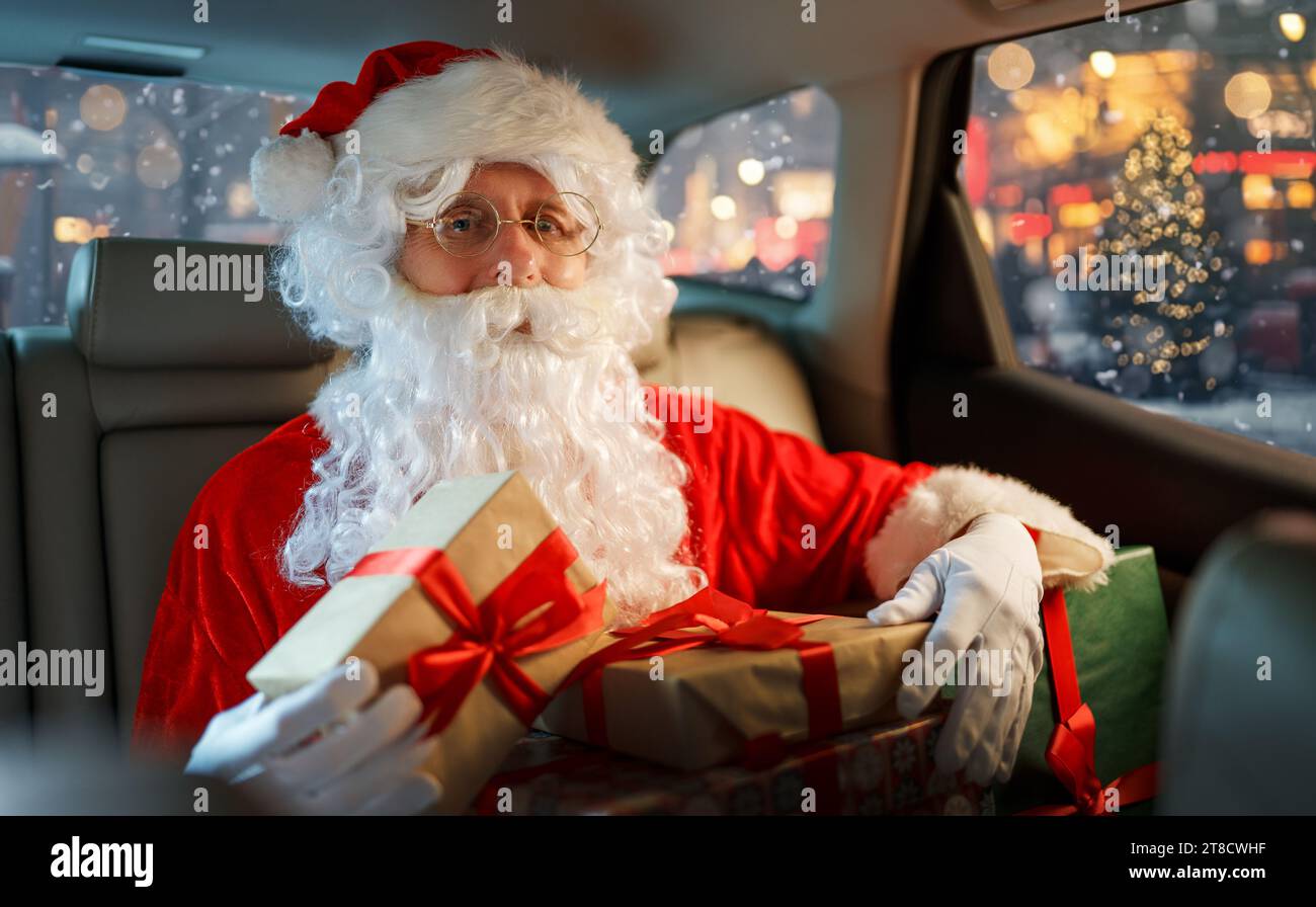 Der Weihnachtsmann hält Geschenke und sitzt im Auto. Feiertagskonzept. Heiligabend. Stockfoto