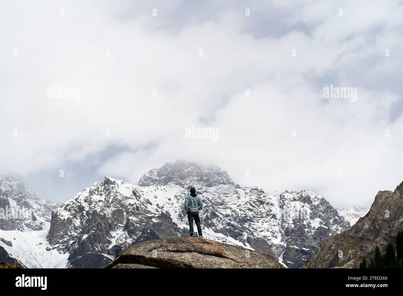 Rückansicht eines männlichen Reisenden aus asien, der auf einem Felsen steht und auf einen Schneeberg in Xinjiang, China, blickt Stockfoto