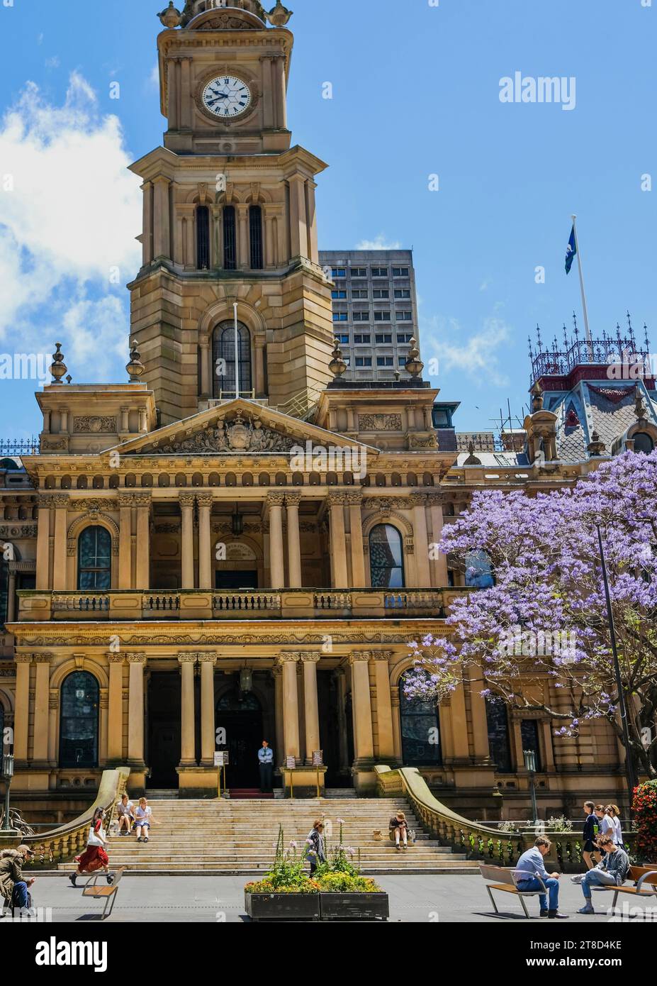 Sydney, New South Wales, Australien - 11. Oktober 2022: Fußgänger spazieren vorbei an Sydney Town Hall und einem blühenden Jacarandabaum, George St Stockfoto