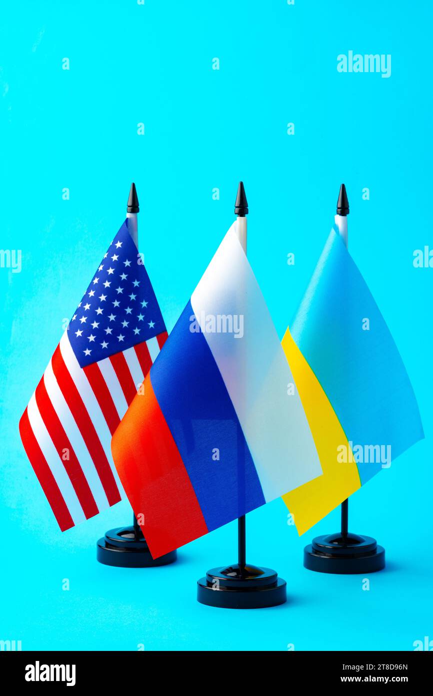 Kleine Fahnen von Russland, der Ukraine und den USA auf blauem Hintergrund Stockfoto