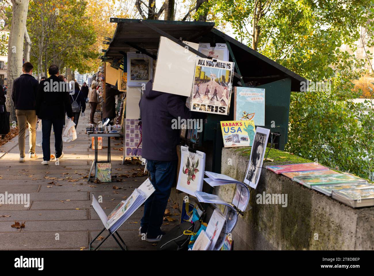 Die Leute schauen sich Bücher und Plakate an, während sie am 19. November 2023 an einem Bouquinisten-Stand vorbeilaufen, der antike Bücher und alte Plakate in der Nähe des seine-Ufers in Paris verkauft. Die Pariser Buchhändler, die größte Open-Air-Buchhandlung der Welt, die seit 450 Jahren am Ufer der seine tätig ist, weigern sich, von den Behörden zur Sicherheit der Eröffnungszeremonie der Olympischen Spiele 2024 in Paris bewegt zu werden. Die 240 Bouquinisten, die auf mehr als drei Kilometern der seine errichtet und zum UNESCO-Weltkulturerbe erklärt wurden, nutzen 900 grüne Boxen, um etwa 300.000 alte Bücher zu beherbergen Stockfoto