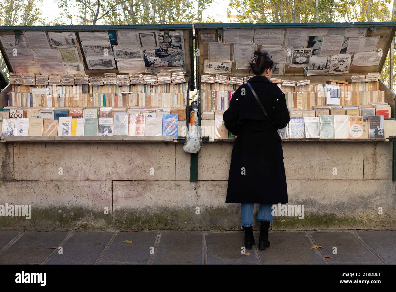 Die Leute schauen sich Bücher und Plakate an, während sie am 19. November 2023 an einem Bouquinisten-Stand vorbeilaufen, der antike Bücher und alte Plakate in der Nähe des seine-Ufers in Paris verkauft. Die Pariser Buchhändler, die größte Open-Air-Buchhandlung der Welt, die seit 450 Jahren am Ufer der seine tätig ist, weigern sich, von den Behörden zur Sicherheit der Eröffnungszeremonie der Olympischen Spiele 2024 in Paris bewegt zu werden. Die 240 Bouquinisten, die auf mehr als drei Kilometern der seine errichtet und zum UNESCO-Weltkulturerbe erklärt wurden, nutzen 900 grüne Boxen, um etwa 300.000 alte Bücher zu beherbergen Stockfoto