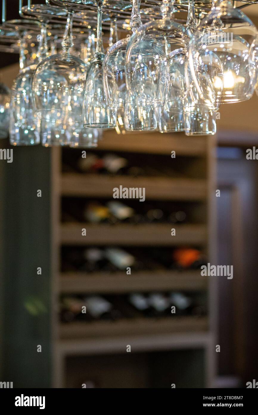 Saubere Weingläser, die über der Bar hängen, auf unscharfem Hintergrund mit einem Regal mit Flaschen Wein Stockfoto