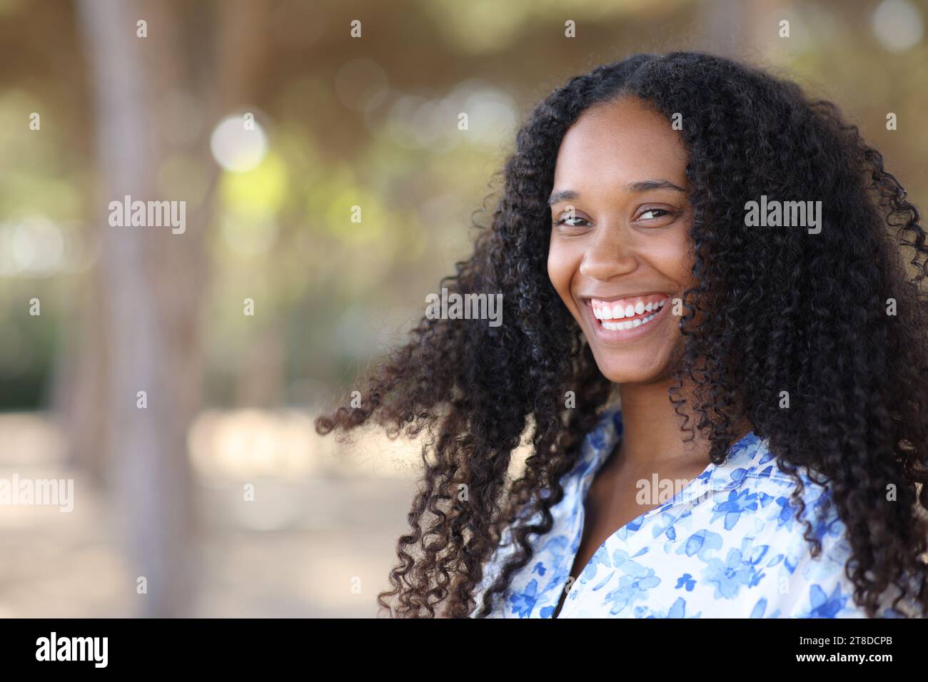 Porträt einer glücklichen schwarzen Frau, die dich mit perfekten Zähnen in einem Park anlächelt Stockfoto