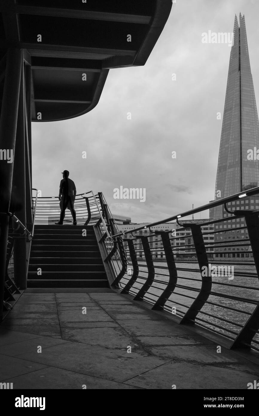 Schwarz-weiß-Bild der Silhouette eines Mannes, der über die Außentreppen geht, mit Londons Symbol, The Shard im Hintergrund. Stockfoto